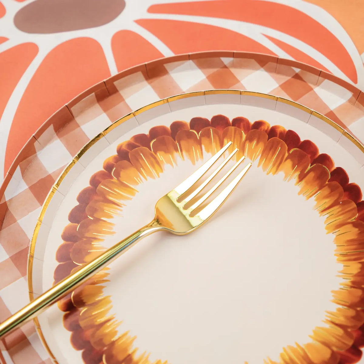 Closeup of a brown and white watercolor plaid paper plate with matching feather plate and pumpkin charger plate.