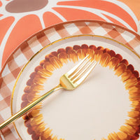 A white paper dessert plate with brown and gold feather design paired with a plaid paper paper plate.