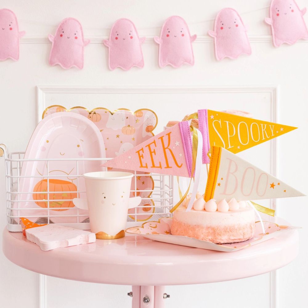 A complete Halloween party setup showcasing pink Halloween paper plates, a ghost-themed cup, and cute spooky decorations, all in pink.