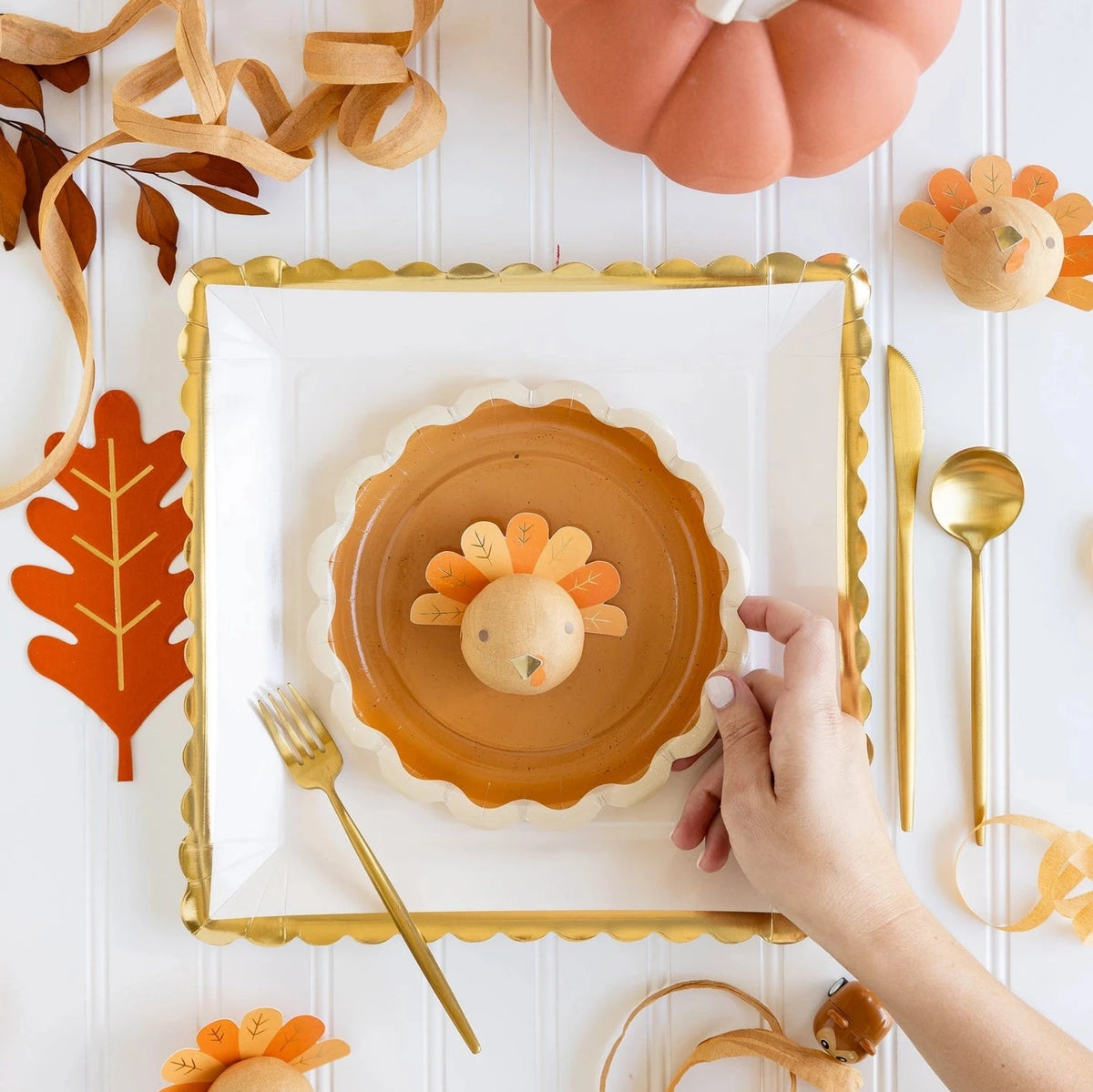 A well-decorated Thanksgiving place setting, featuring scalloped plates, wooden turkey decor, and an orange oak leaf-shaped Thanksgiving Paper Napkin.