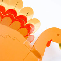 Close-up of a vibrant paper plate turkey showing detailed feathers in autumn shades with gold foil accents. Perfect for serving festive desserts at any Thanksgiving gathering.