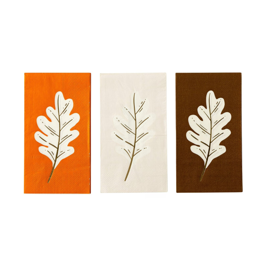 Set of three fall napkins in orange, cream, and brown, each featuring a gold foil oak leaf design. A stylish addition to any Thanksgiving tableware or party decorations.