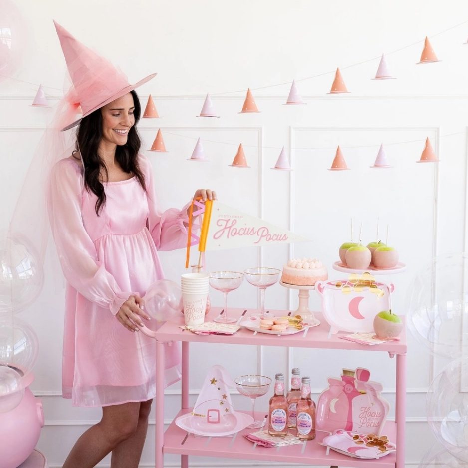 Woman in pink dress setting up a Halloween party with Hocus Pocus decor, featuring pink Halloween decor and a party in a box setup.