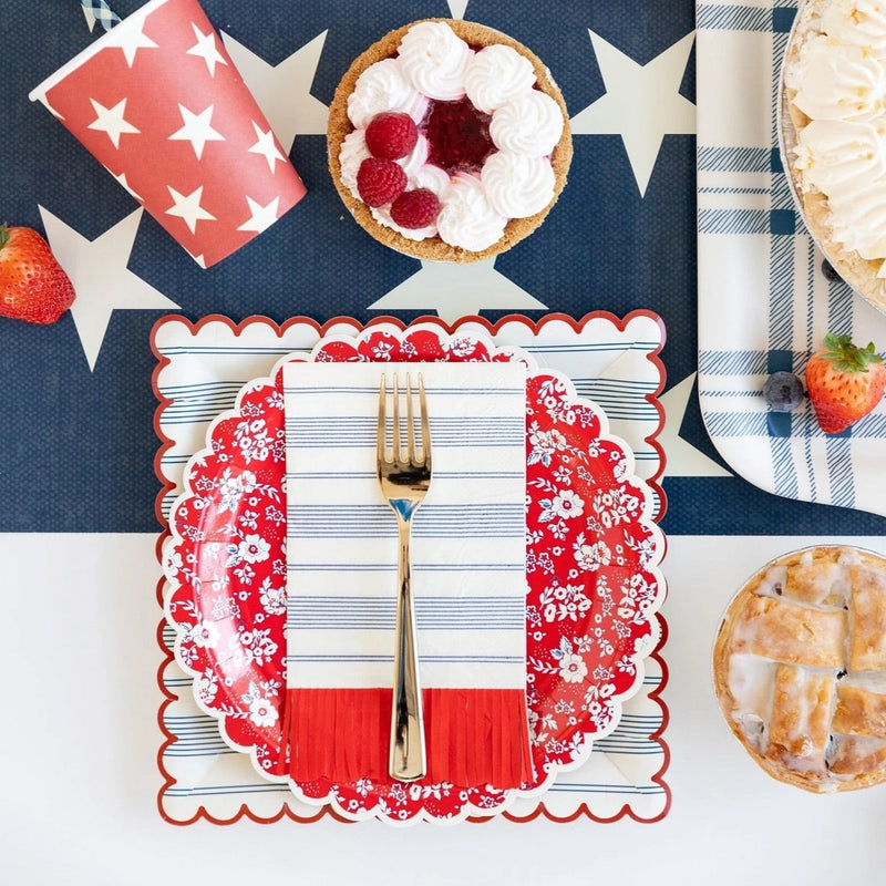 Blue striped paper dinner napkins with red scalloped fringe edge on a patriotic table.
