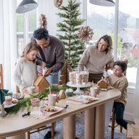 a family decorating gingerbread houses around a table featuring a tan and white Checkered paper table runner 