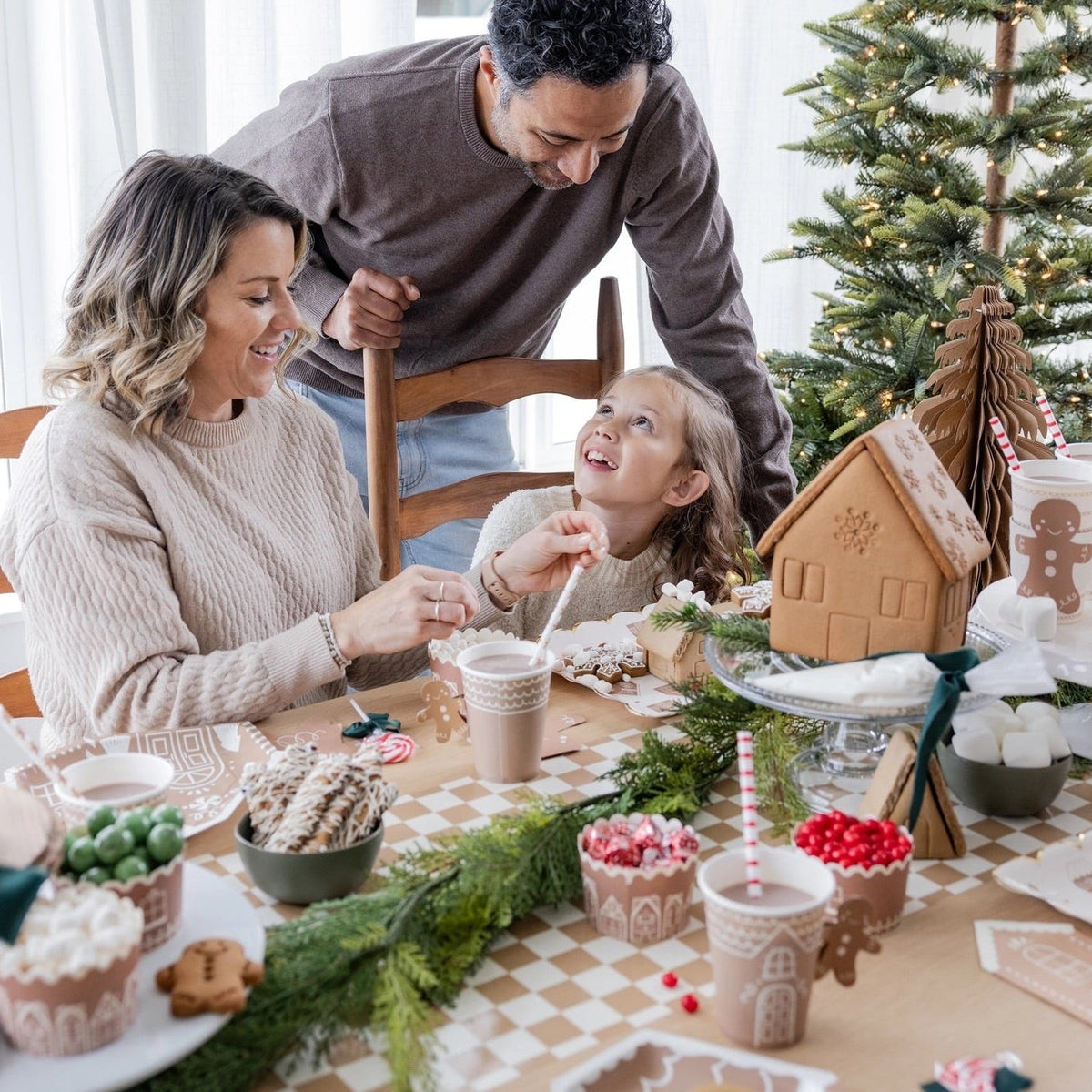 a family decorating gingerbread houses around a table featuring a tan and white Checkered paper table runner 