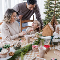 a family decorating gingerbread houses around a table featuring a tan and white Checkered paper table runner 