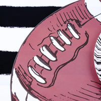 Close-up of a brown and white football placemat showing detailed laces on a black and white striped background. Ideal for football party decor.