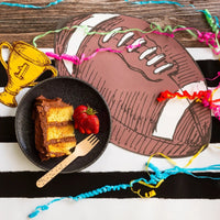 Football placemat on a striped black and white table runner, topped with a plate of cake, strawberries, and colorful party streamers. Perfect football party decor.