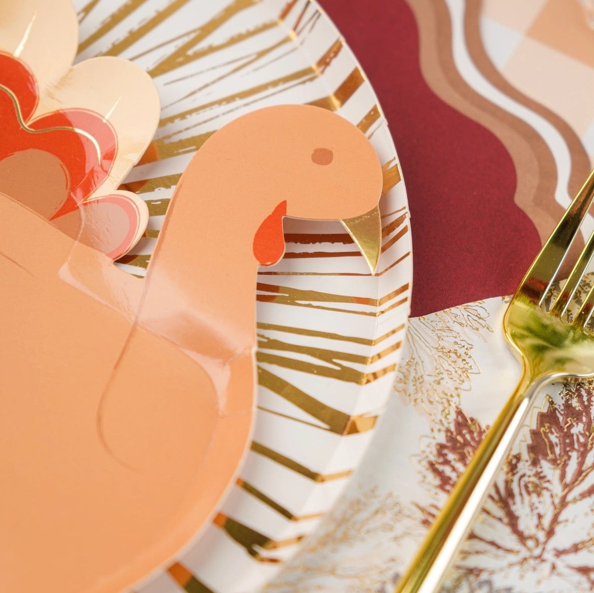 Thanksgiving table setting featuring a white and gold foil dinner paper plate, complemented by a turkey-themed decor. These 10.5-inch gold paper plates are eco-friendly, perfect for Thanksgiving dinner, adding a festive flair to your holiday table.