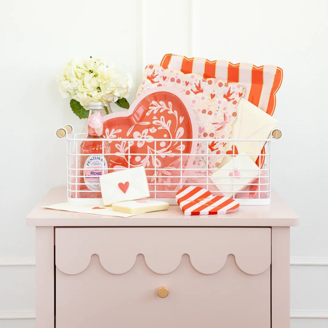 Pink and red be mine valentines day napkins shaped like a heart with coordinating of valentines day party decor in a white basket