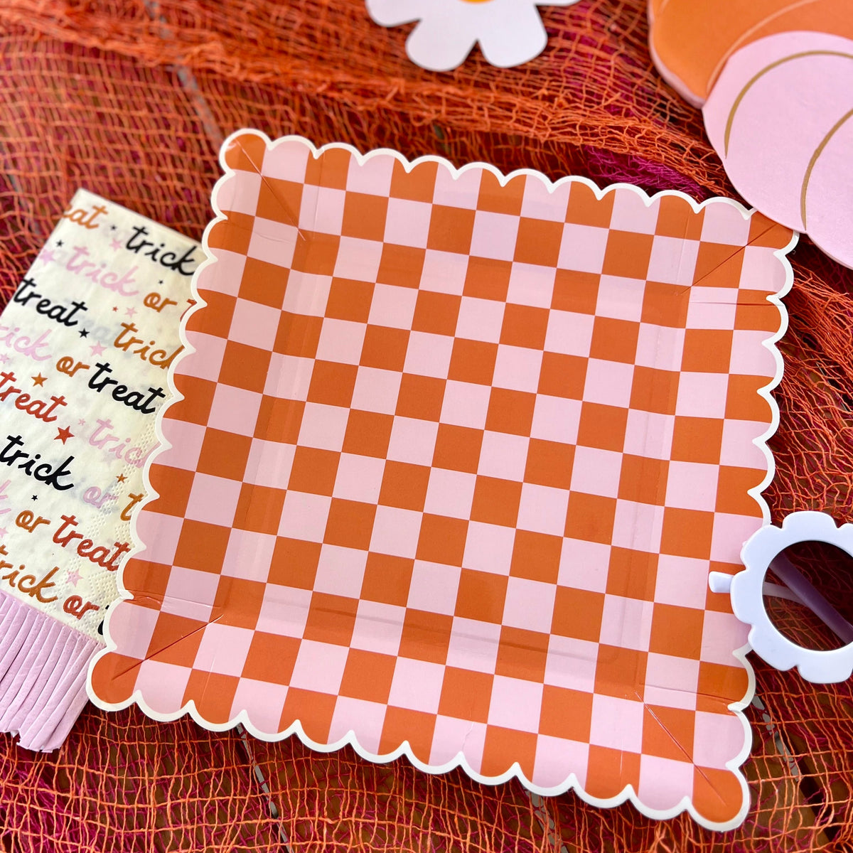 A close-up of an orange and pink checkered Halloween plate, paired with 'Trick or Treat' napkins and other Halloween table decorations.