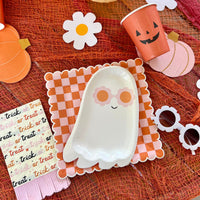 A Halloween table setting featuring an orange and pink checkered plate, surrounded by playful Halloween decor including pumpkin cups and ghost plates.