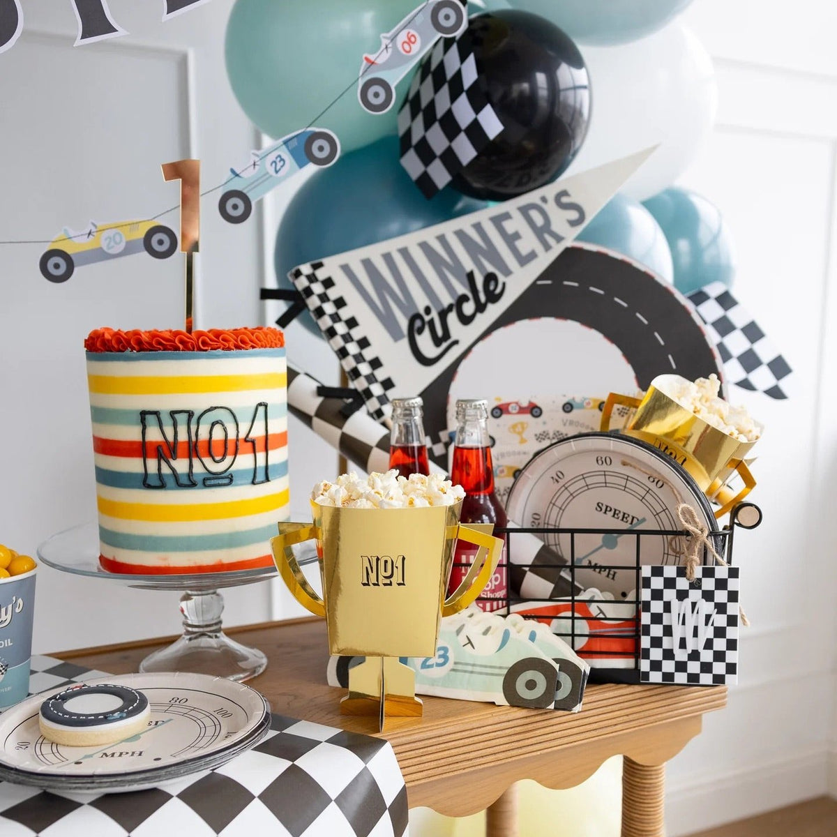 Full race car-themed birthday party table setup featuring speedometer plates, trophy decorations, and checkered balloons.