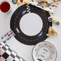 Overhead view of speedometer plates on a race track table setting with colorful car-themed party decor and themed snacks.