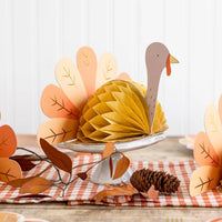 A Thanksgiving table setting featuring multiple honeycomb turkey centerpieces with orange and cream tail feathers, adding a festive touch to the holiday decor