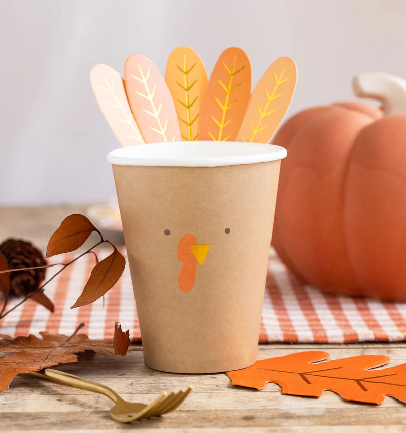 A charming paper turkey cup with assembled feather accents, set on a Thanksgiving kids table alongside autumnal decor and treats, making the perfect festive touch for the holiday celebration.