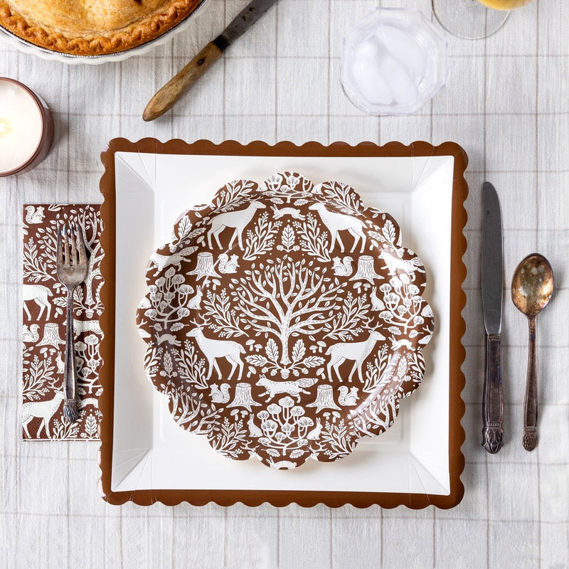 A beautifully set Thanksgiving table featuring a brown toile plate and matching Thanksgiving napkin with woodland animal and tree motifs. The fall napkins add a rustic yet elegant touch, perfect for autumn gatherings.