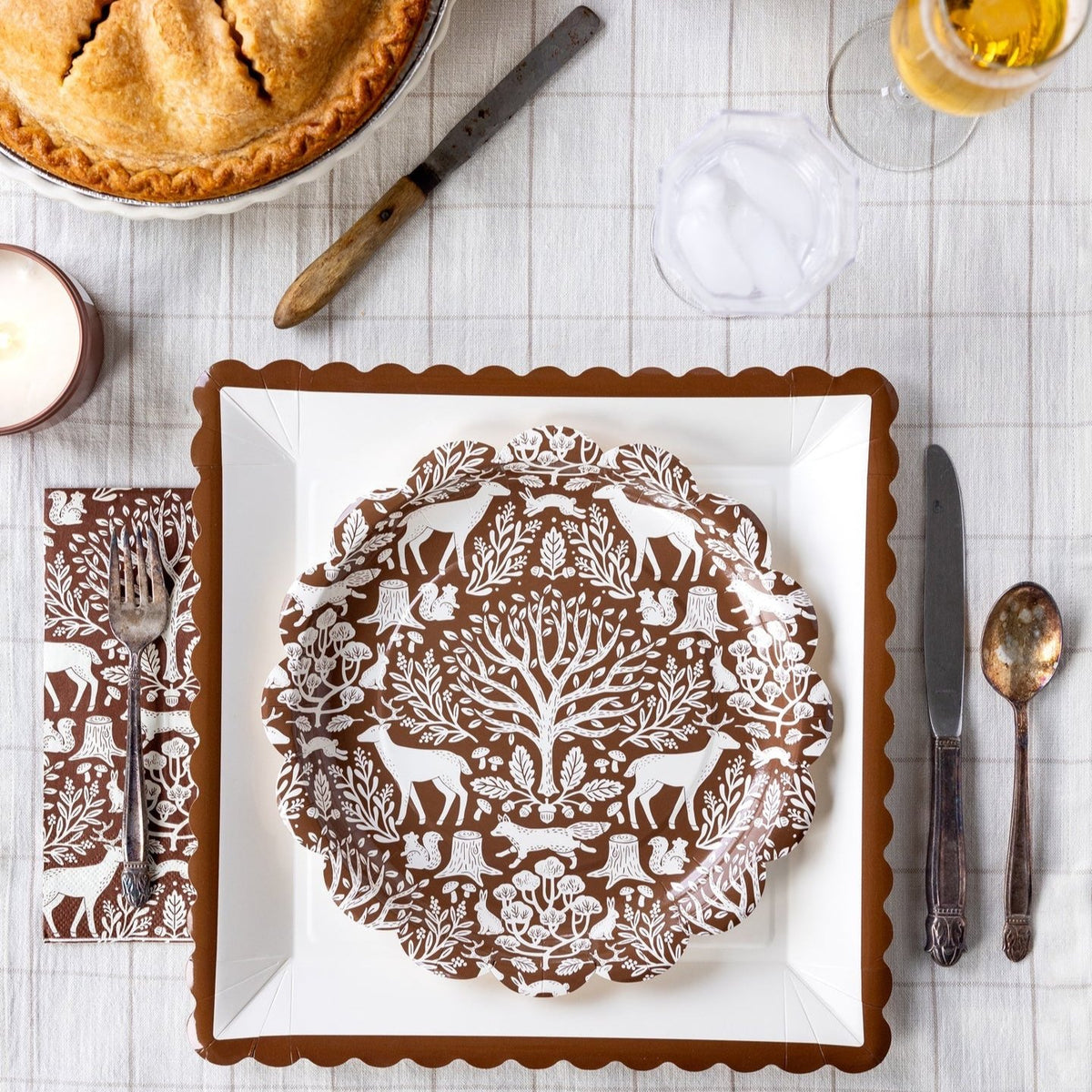 A beautifully set Thanksgiving table featuring a brown scalloped-edge paper plate, a turkey-themed place setting, and festive fall decorations. Perfect for adding a touch of elegance to your Thanksgiving feast.