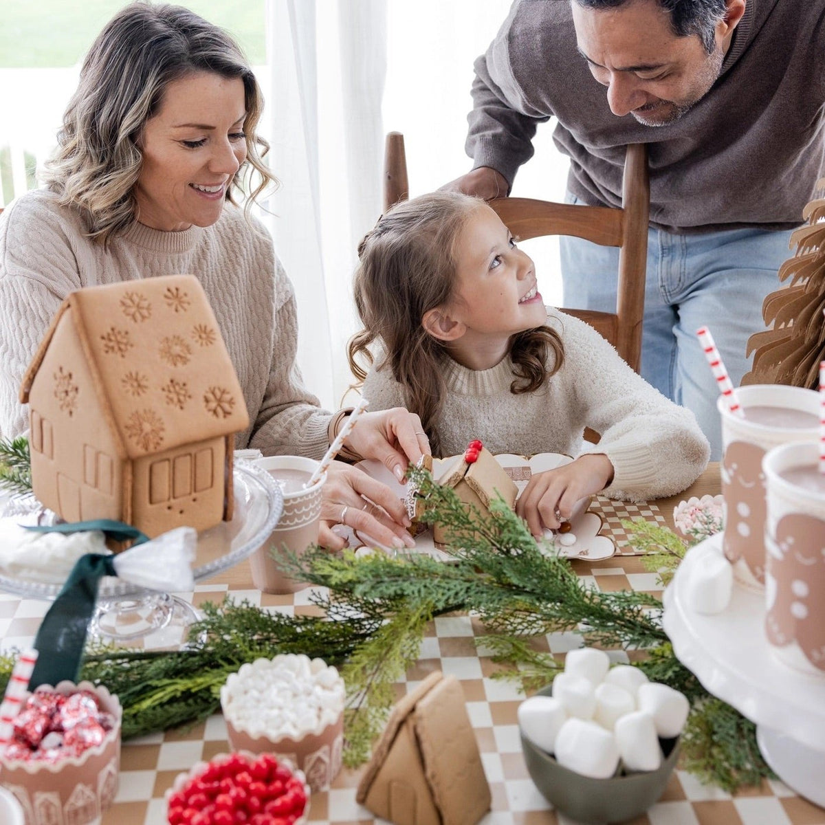 a family decorating gingerbread houses around a table featuring a tan and white Checkered paper table runner 