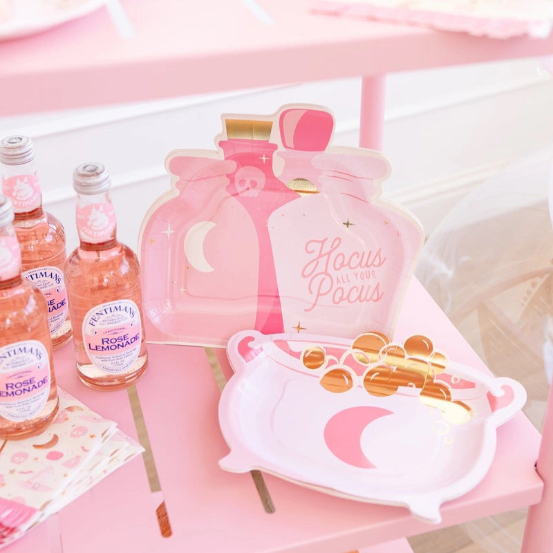 Pink potion bottle-shaped Halloween paper plates on a pink table setup with rose lemonade bottles.