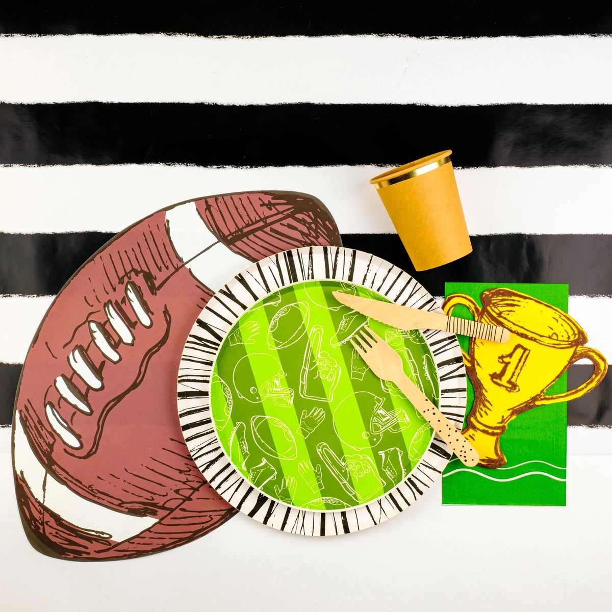 Football placemat paired with a green football-themed plate, wooden cutlery, and a golden trophy cutout on a black and white striped table runner. Essential football party decor.