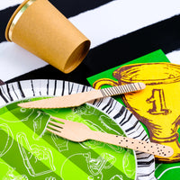 Close-up of a green plate, golden trophy-shaped paper napkin, and wooden cutlery on a striped table runner, ideal for a sports themed birthday party.