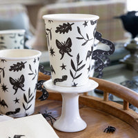 Set of 8 white paper Halloween cups with black designs of bats, snakes, and spooky plants, each with an adhesive black snake-shaped handle.