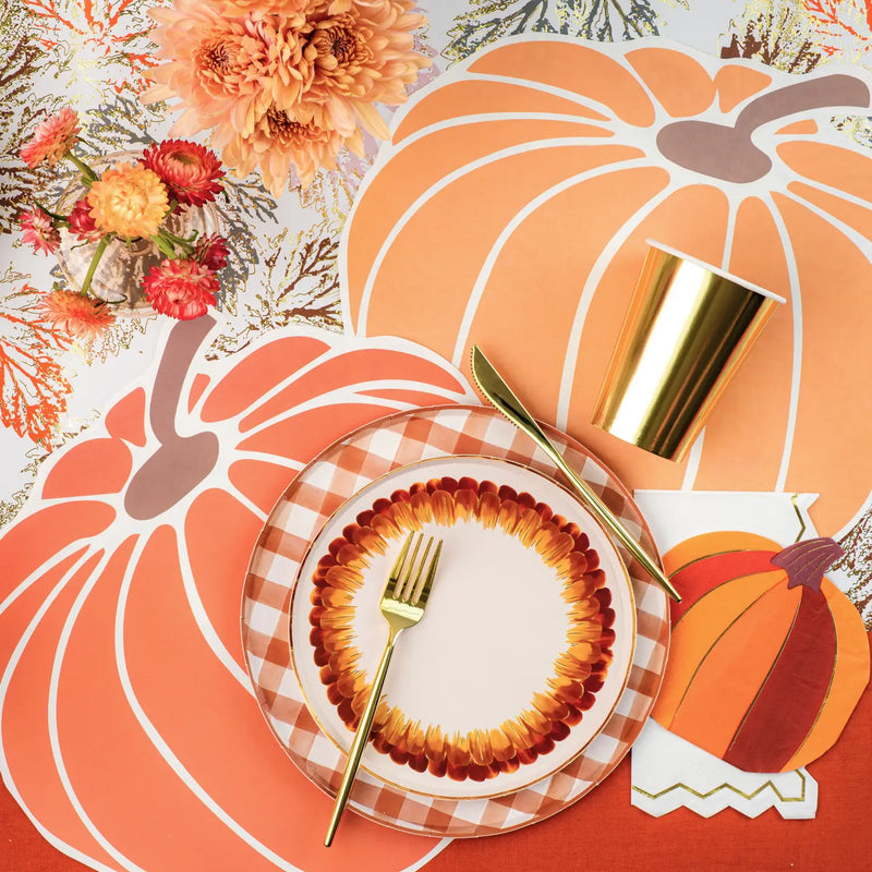 A white paper dessert plate with brown and gold feather design on a Thanksgiving table setting.