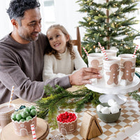 a family decorating gingerbread houses around a table featuring a tan and white Checkered paper table runner 