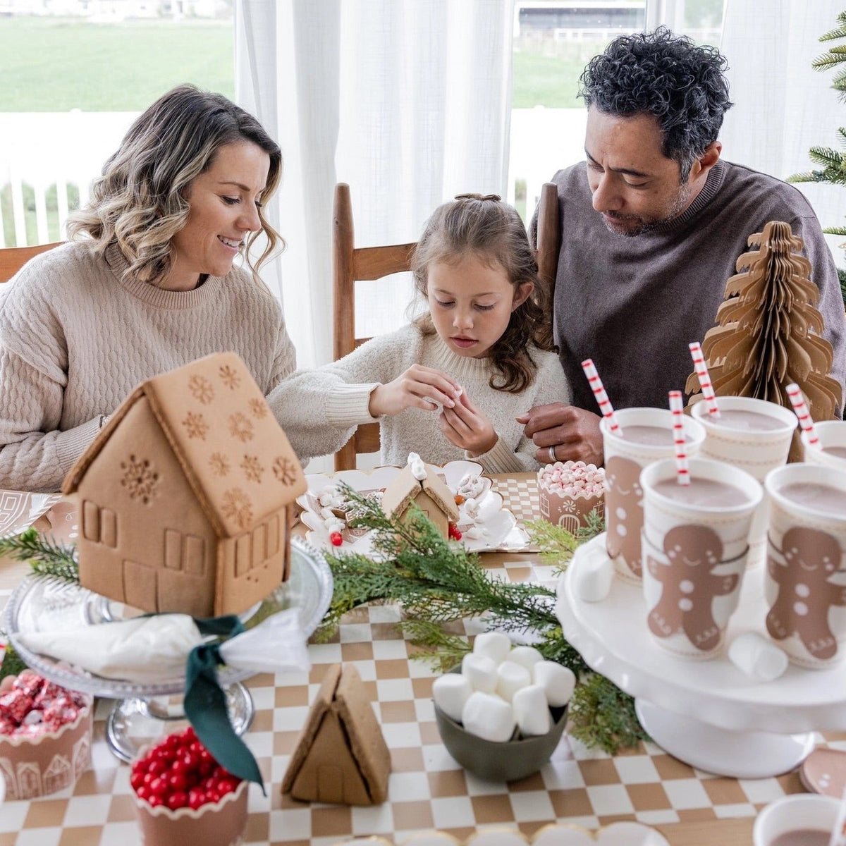 a family decorating gingerbread houses around a table featuring a tan and white Checkered paper table runner 