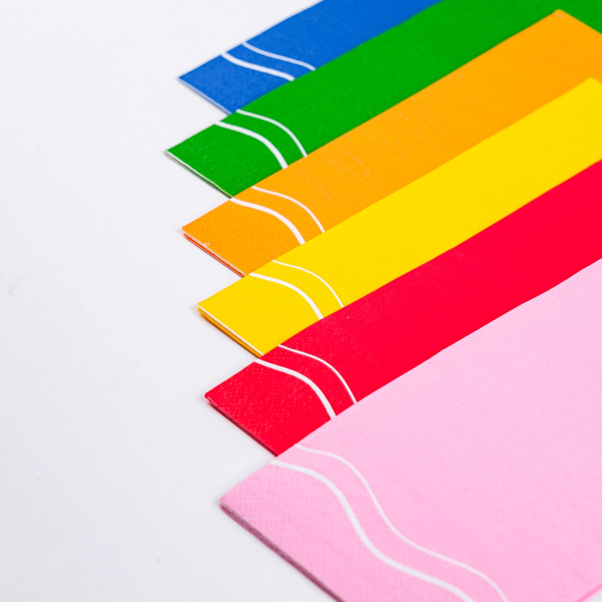 Close-up of colorful paper guest towels in green, blue, orange, yellow, red, and pink, each with a decorative white wavy line, ideal for rainbow party supplies or festive gatherings.