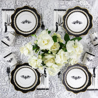  beautifully arranged Halloween party table showcasing classy Halloween decorations with matching black-and-white Halloween paper napkins, bat-themed plates, and floral centerpieces. This setup adds sophistication to your Halloween decor.