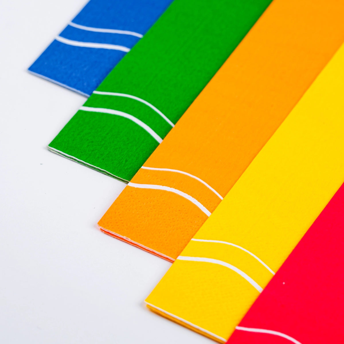 A row of vibrant paper guest towels in various colors including green, blue, yellow, orange, red, and pink, each with a simple white wavy line, great for decorative paper napkins at any celebration.