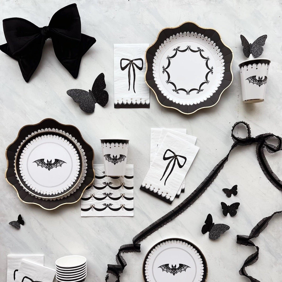 A flat lay showcasing elegant Halloween decorations, including a large black-and-white Halloween plate with a bat design, matching cups, and napkins. Perfect for a spooky yet refined Halloween celebration.